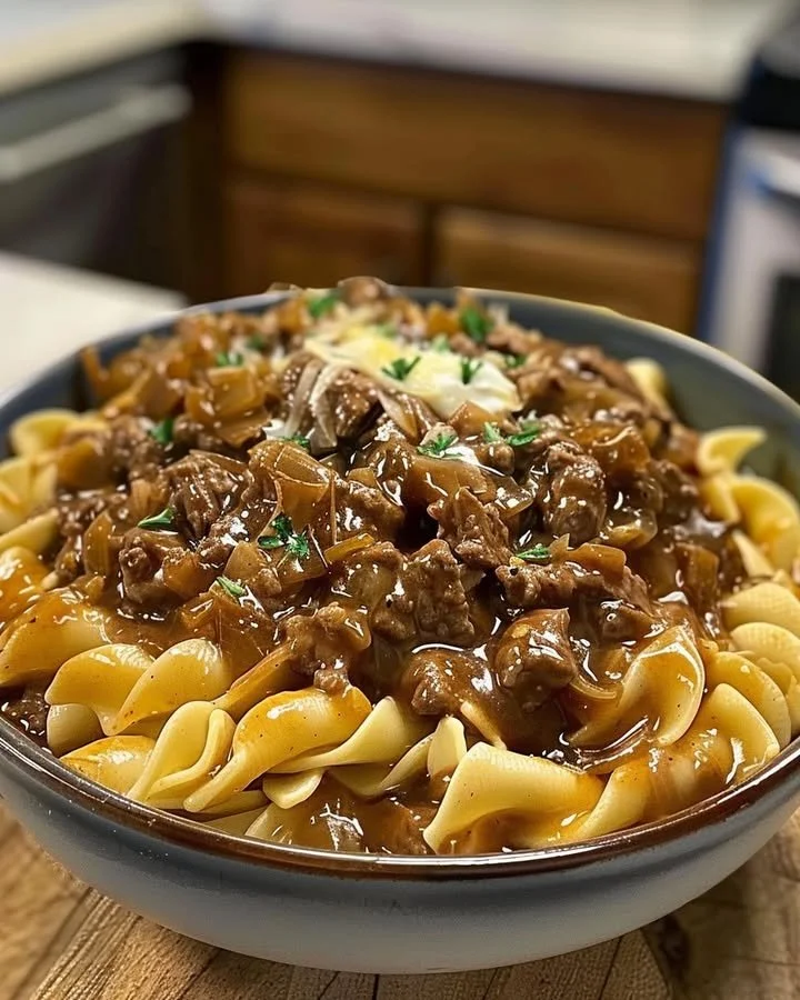 Delicious bowl of French onion beef and noodles topped with melted cheese and herbs.