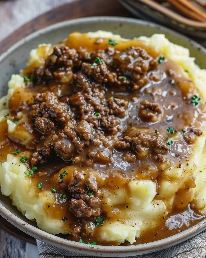 Ground beef and gravy dish served on mashed potatoes, garnished for presentation.