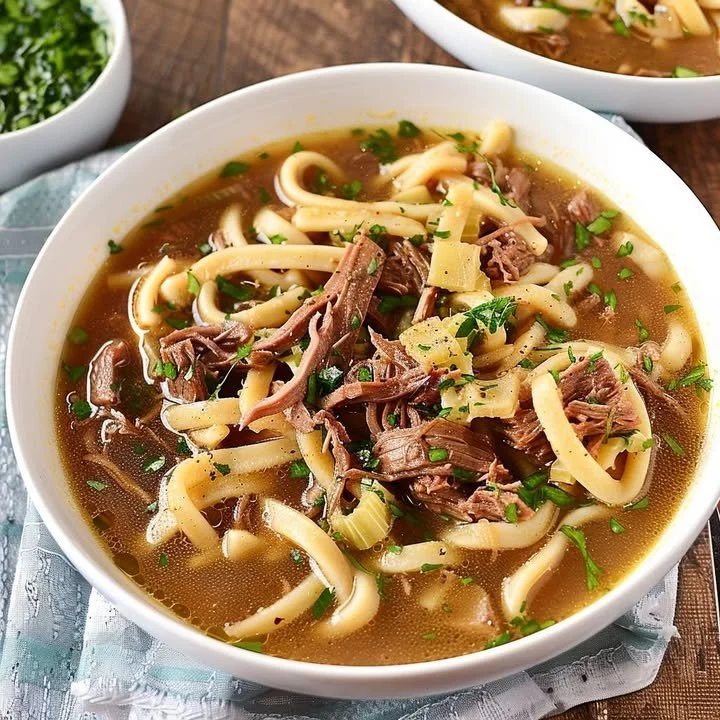 Bowl of slow-cooked beef noodle soup with fresh herbs and noodles
