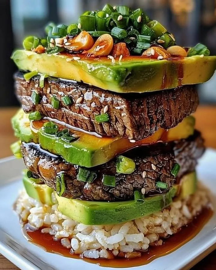 Teriyaki beef and avocado rice stack served on a plate with fresh ingredients.