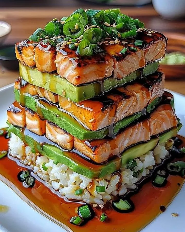 Teriyaki salmon avocado rice stack served in a bowl, garnished with sesame seeds.